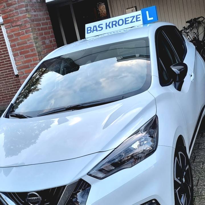 Het dakbord met BAS KROEZE en het blauwe L-bordje op de witte lesauto in Weert