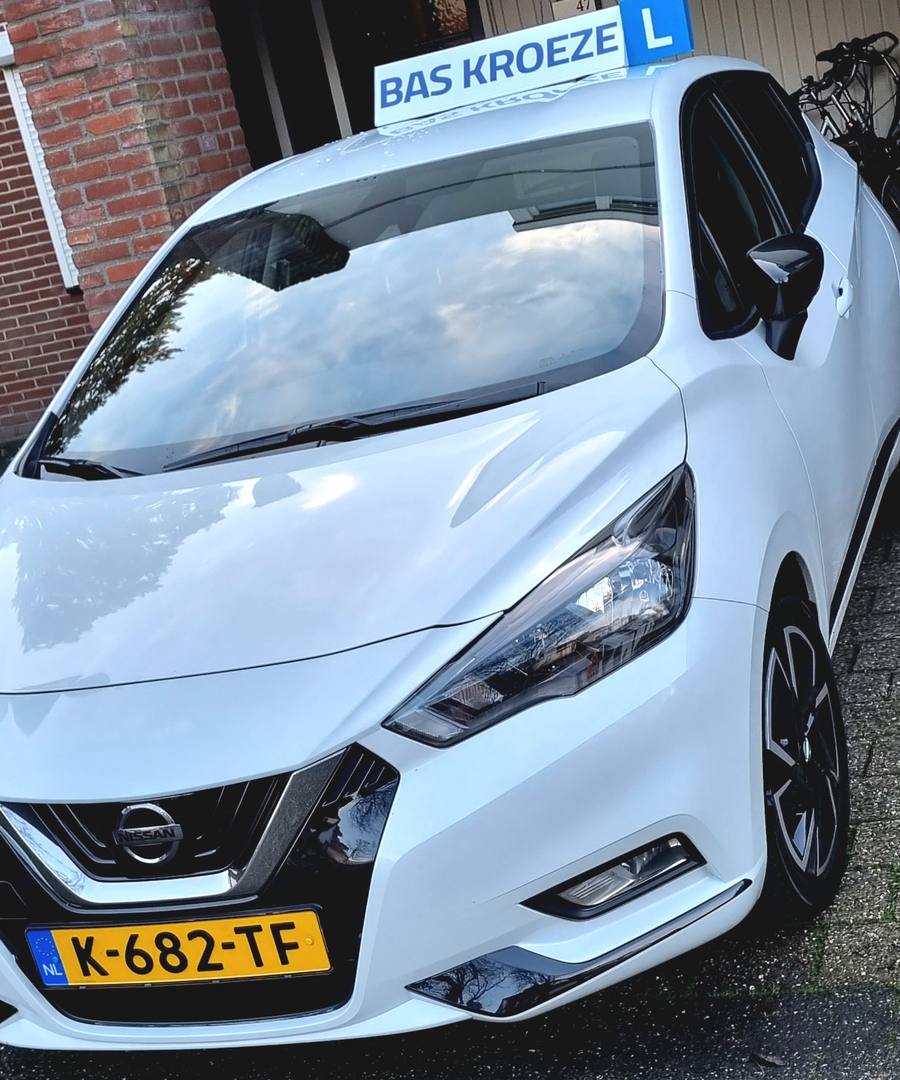 De witte lesauto van Autorijschool Bas Kroeze met het dakbord BAS KROEZE en het blauwe L-bordje, voor de deur aan de Leukerhof in Weert